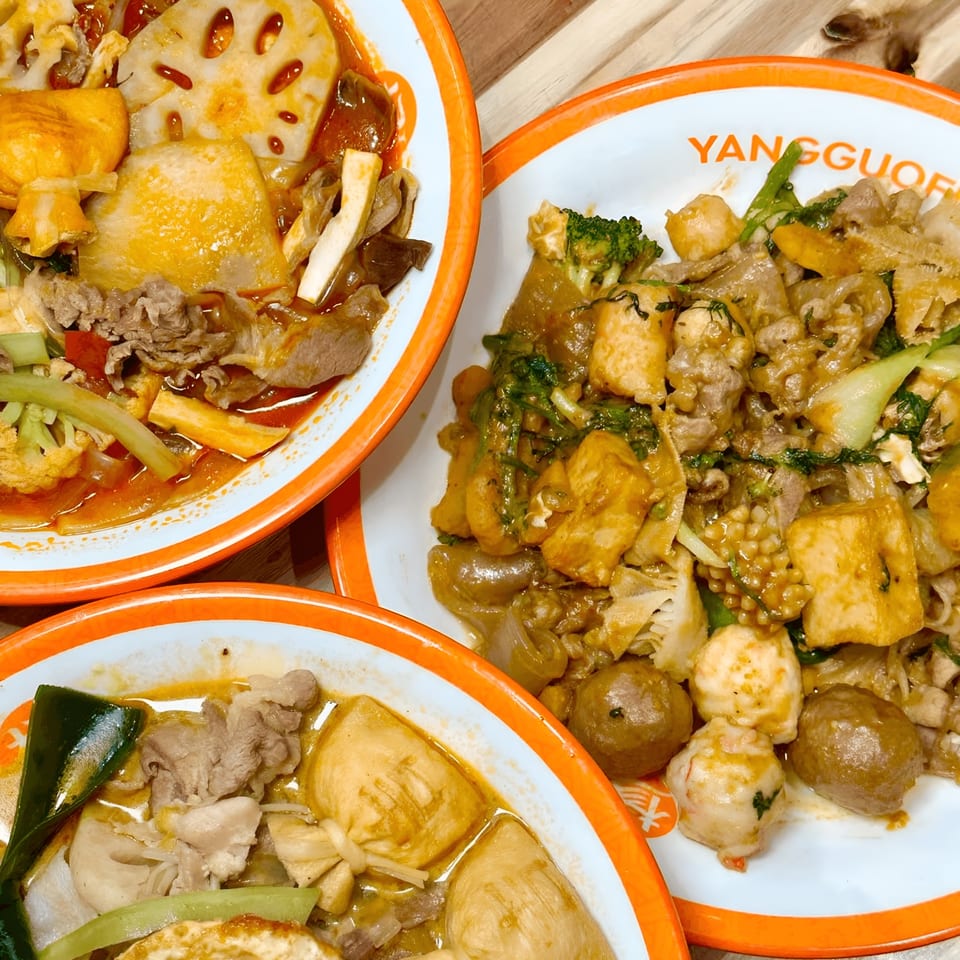 Three bowls of YGF Malatang, two with spicy broth and one with a savory sauce, filled with various ingredients.