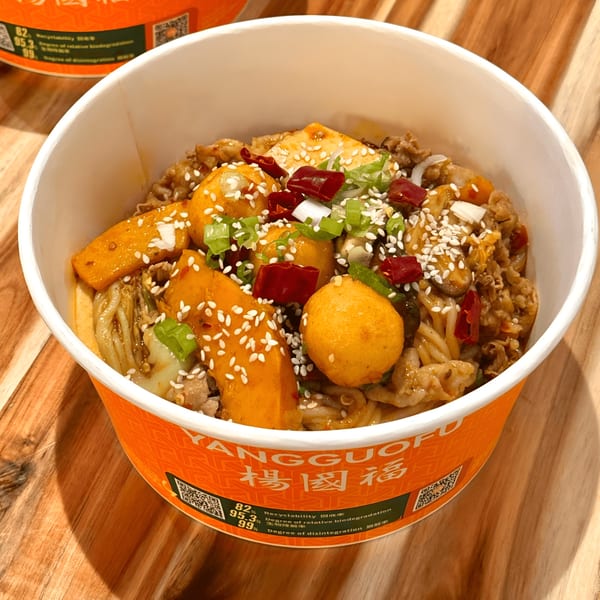 A YGF Malatang bowl filled with noodles, meat, fish balls, vegetables, chili, and sesame seeds.
