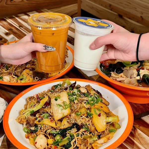 Two hands clinking drinks above three bowls of YGF Malatang's Chinese noodle dishes.