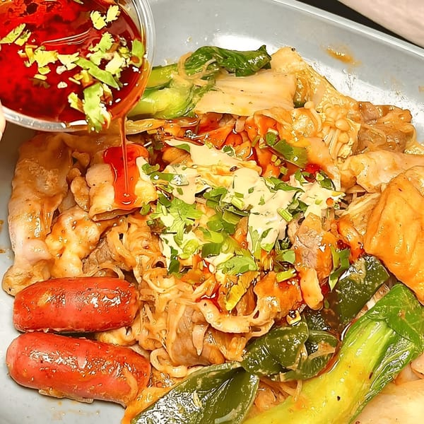 Spicy red sauce with cilantro being poured over a bowl of YGF Malatang with various ingredients.