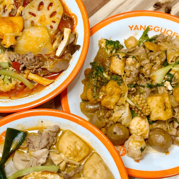 Three bowls of YGF Malatang, two with spicy broth and one with a savory sauce, filled with various ingredients.